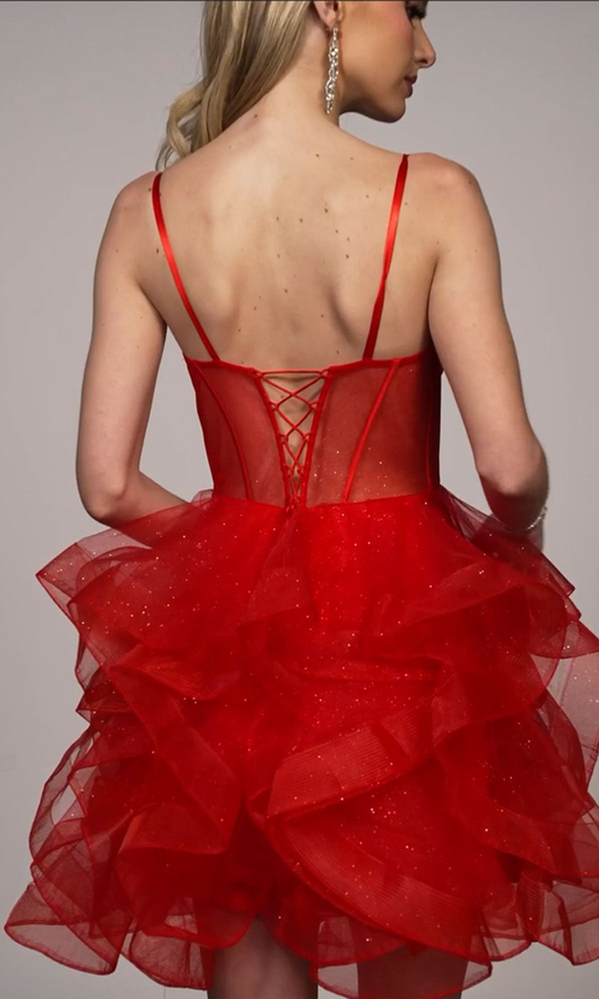 Woman wearing the Dave & Johnny Short Red Ruffle Hoco Dress 11827, featuring spaghetti straps, a lace-up back, and a layered ruffled skirt, posed from behind against a neutral background.